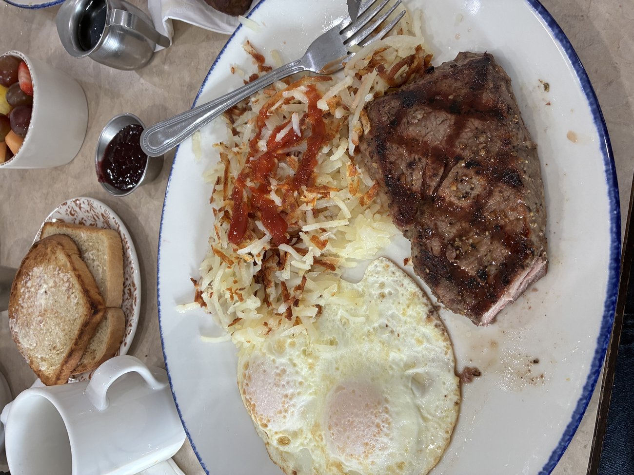 A grilled steak with a fried egg, hashbrowns, toast and fruit