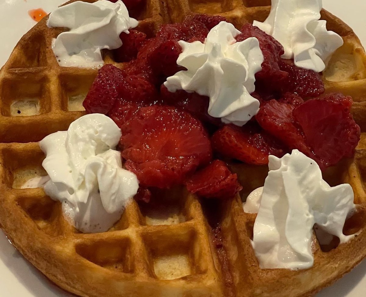 A Belgian waffle topped with strawberries and whipped cream